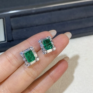 Close-up of hand holding emerald-cut silver earrings with rectangular halo diamond setting