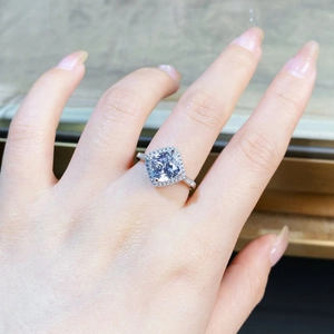 Gros plan d'une bague halo diamant coussin au doigt avec anneau pavé en argent