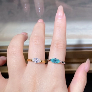 Detail of silver and gold marquise cut rings with teal and clear moissanite stones