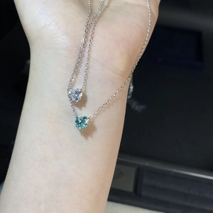 Gros plan de pendentifs moissanite en forme de cœur en argent et bleu sarcelle sur main