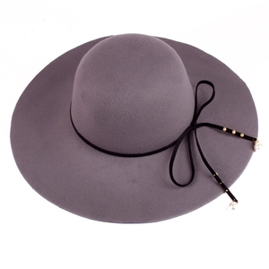 Detail of grey wool fedora hat featuring black ribbon bow with pearl and gold pendant