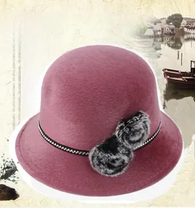 Gros plan sur un chapeau cloche rose foncé avec des pompons décoratifs en fausse fourrure bicolore