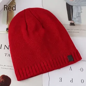 Red knit beanie hat with ribbed cuff and leather logo patch on minimalist background