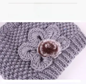 Detailed view of grey winter knit hat with a large 3D flower and fluffy pompom accent