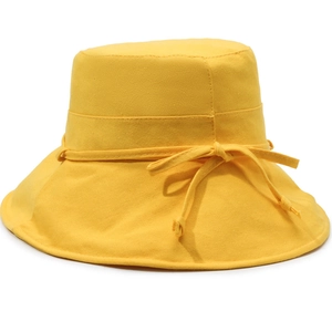 Detail view of a yellow canvas bucket hat with a decorative matching bow on the side