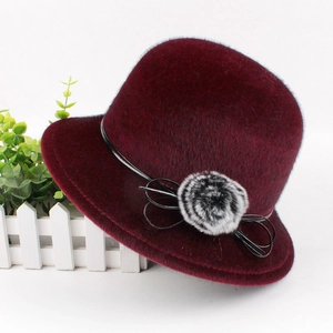 Detail of burgundy faux mink fur hat featuring a black ribbon bow and fluffy pom-pom