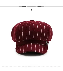 Detail of burgundy newsboy hat with white vertical stripes and crystal letter pin