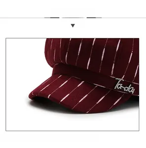 Close-up of burgundy newsboy hat with white dotted stripes and rhinestone logo detail
