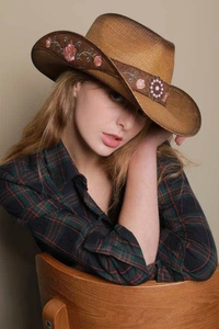 Close-up of pink rose embroidery and vintage metal ornaments on a straw cowboy hat