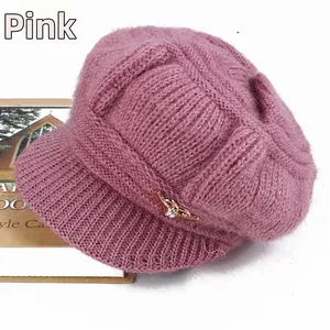 Detail of dusty pink knitted peak cap with plush fleece texture and gold bow ornament
