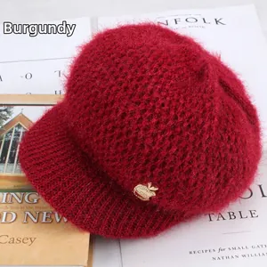 Detail of burgundy mohair knit cap with a golden apple buckle on minimalist background