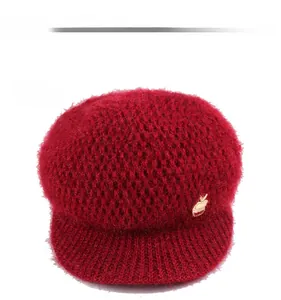 Detailed texture of burgundy knitted beret with fuzzy mohair-like wool and gold apple badge