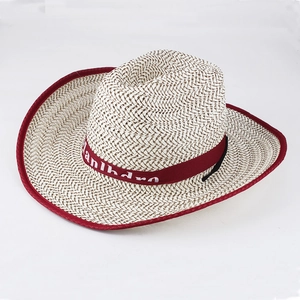 Detail of beige straw cowboy hat with dark red brim and lettered decorative ribbon