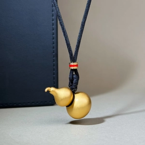 Pendentif gourde en or mat avec cordon noir sur fond de cuir bleu foncé élégant