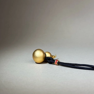 Détail du pendentif Hulu en or mat avec cordon tressé noir et perle rouge