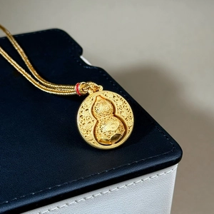 Macro shot of rotatable gold gourd pendant with intricate cloud patterns and red bead accent