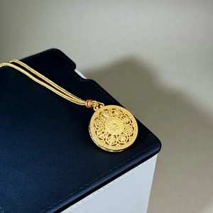 Macro shot of gold pendant with intricate filigree cutouts and red enamel accent