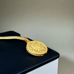 Close-up of golden Fu character pendant with intricate filigree and woven chain