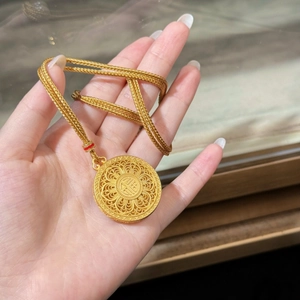 Detailed macro view of a gold Fu pendant with intricate filigree and red accents