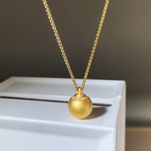 Halskette mit mattgoldem Anhänger und Diamantbesatz auf weißem Schmuckkästchen