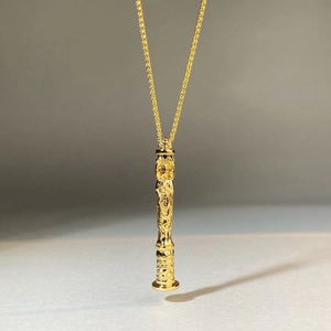 Vue détaillée d'un pendentif cylindrique plaqué or avec de fines gravures religieuses