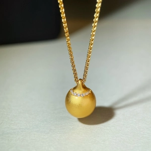 Detail eines mattgoldenen Kugelanhängers mit Kristallinlay an einer Kordelkette