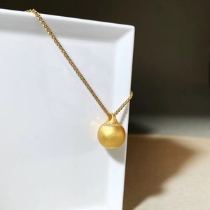 Nahaufnahme von mattgoldener Kugel mit Zirkonkragen an einer goldenen Kordelkette