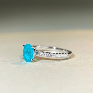 Macro side view of an oval neon blue gemstone ring with pave diamonds on silver band