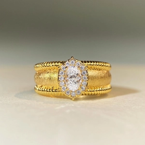 Close-up of gold ring with oval gemstone halo setting and textured rope band