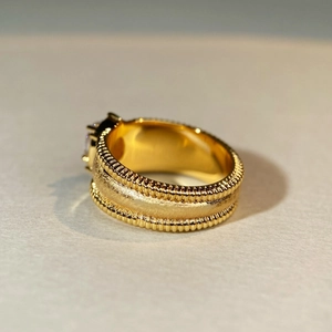 Macro shot of gold wide ring with frosted texture, beaded edges and a clear gemstone