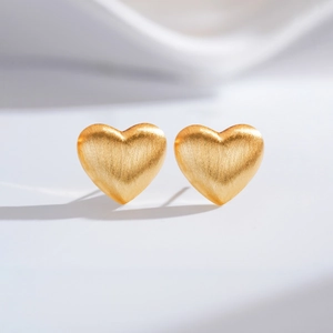 Detail of matte heart-shaped gold earrings with brushed metallic texture and 3D design