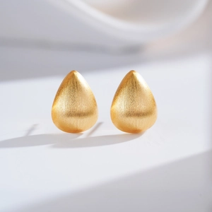 Macro view of gold teardrop earrings featuring a brushed metal texture and matte finish