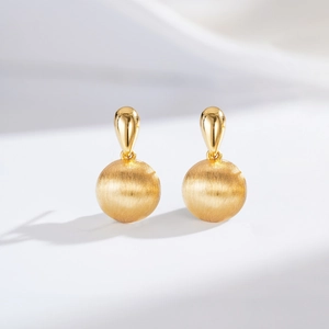 Macro detail of 24K gold-plated drop earrings featuring a matte brushed metal sphere