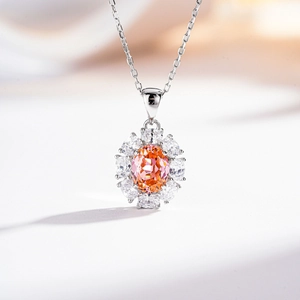 Detail of silver necklace featuring an orange-pink oval gemstone in a petal halo setting
