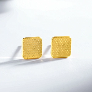 Detailed close-up of golden square stud earrings with textured grid pattern and metallic finish