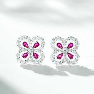 Macro detail of silver four-leaf clover earrings with red pear-shaped gemstones and zircon