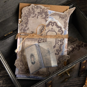Vintage scrapbooking paper set with floral frames and antique newspaper motifs in a wooden box