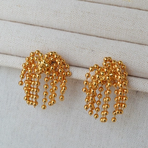 Close-up of golden beaded tassel earrings with multiple metal chains on a fabric stand