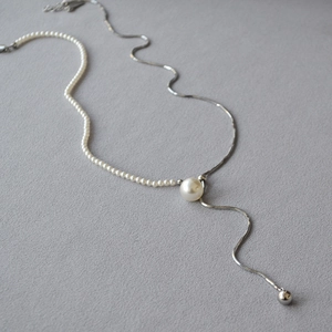 Asymmetrical necklace with pearls and silver snake chain shown on grey fabric
