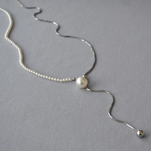Detail of adjustable Y-necklace with pearls and silver snake chain on grey fabric