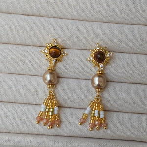 Dettaglio di orecchini vintage placcati oro con pietra occhio di tigre e nappe