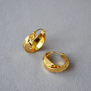 Detail view of gold-plated brass hoop earrings with hammered texture and cross design