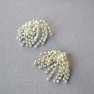 Detail of silver tassel earrings with beaded metal chains on textured background
