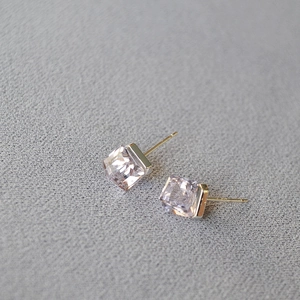 Macro detail of square-cut purple crystal earrings with gold posts on a grey textured fabric
