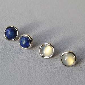 Macro shot of 925 silver stud earrings with lapis lazuli and moonstone on grey fabric