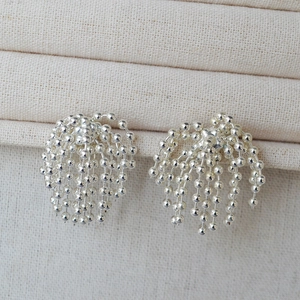 Detail of silver beaded tassel earrings featuring sleek metallic fringe on linen background