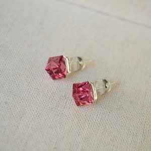 Detail of rose red square crystal earrings with silver base on white linen fabric