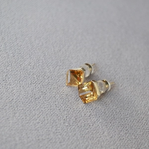 Close-up of amber square crystal stud earrings with gold plating and silicone backs