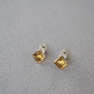 Macro shot of amber square-cut crystal earrings with gold base on textured grey fabric