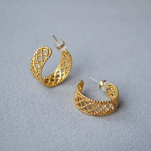 Macro shot of gold-plated C-shape earrings with intricate hollow woven lace texture